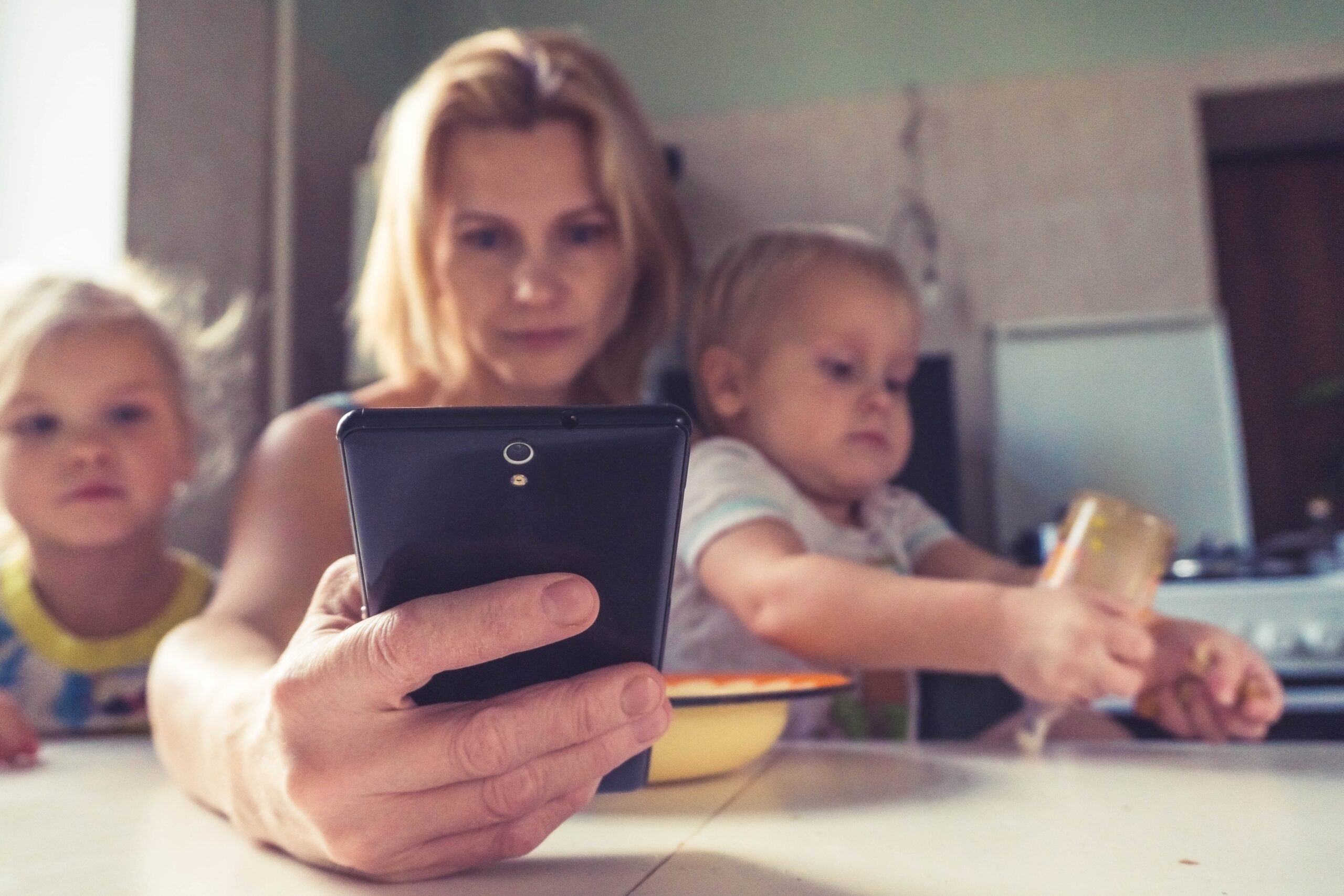 Mother looking at smartphone while baby reaches up for her attention during playtime