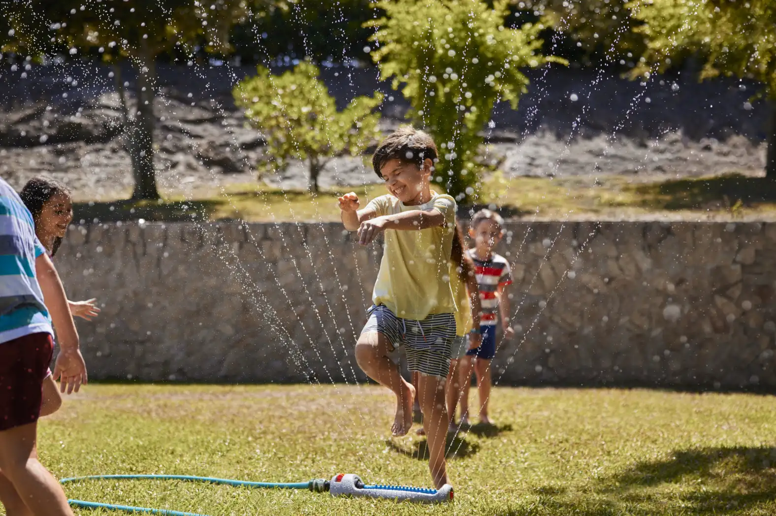 Kids playing tag through sprinkler spray in yard