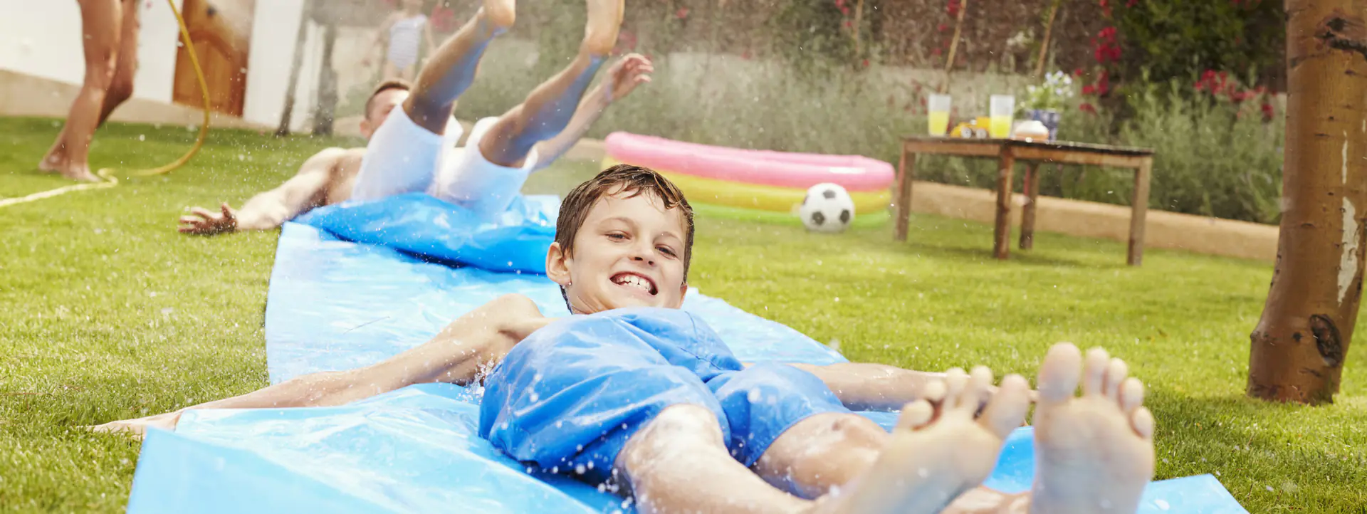 Kids sliding down soapy wet tarp on grassy slope