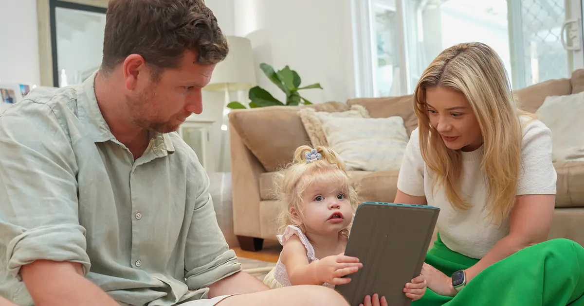 Parent distracted by smartphone while toddler plays alone nearby, illustrating the link between parental screen use and child development