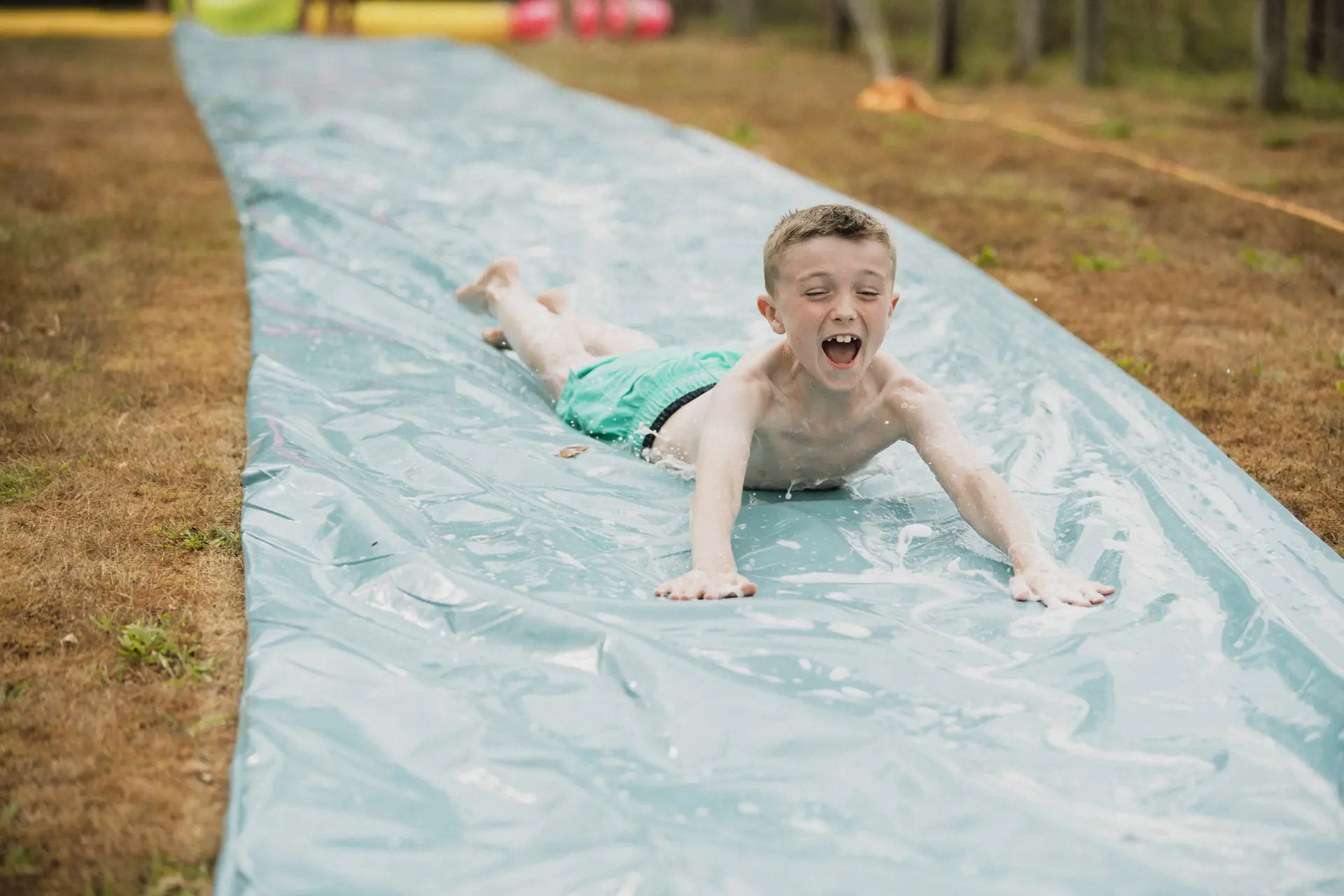 Preschool age kids sliding on wet DIY tarp slide