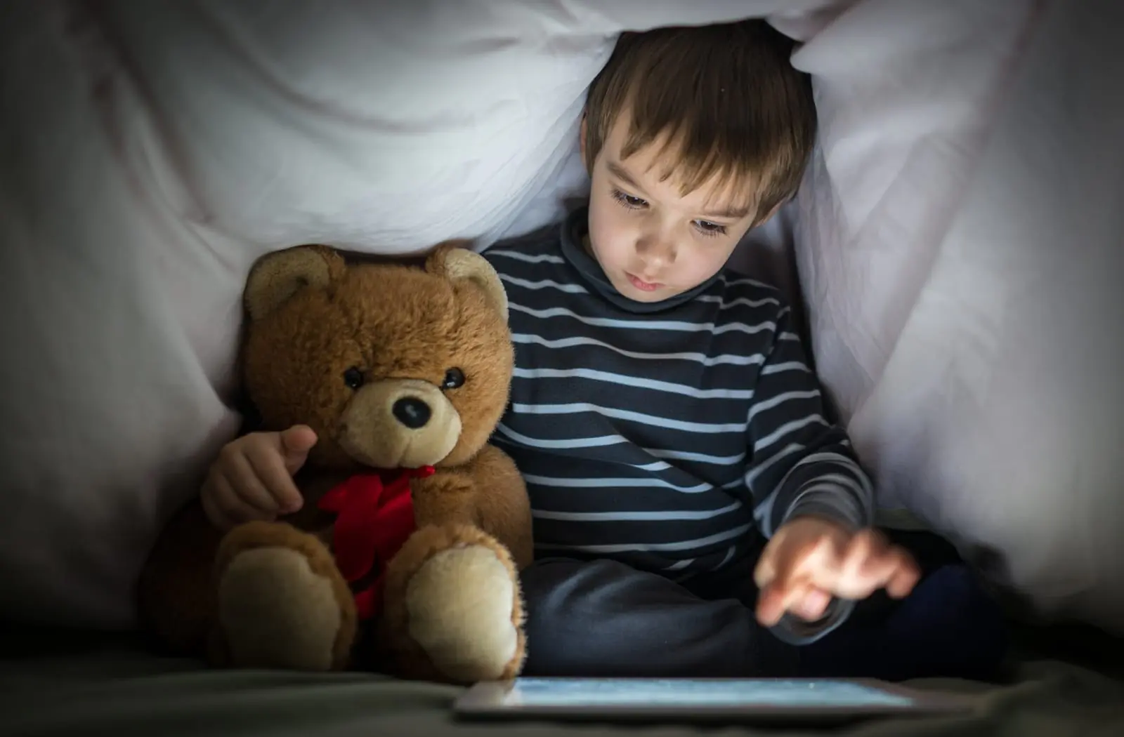 Child lying in bed using tablet or smartphone in dark room before sleep