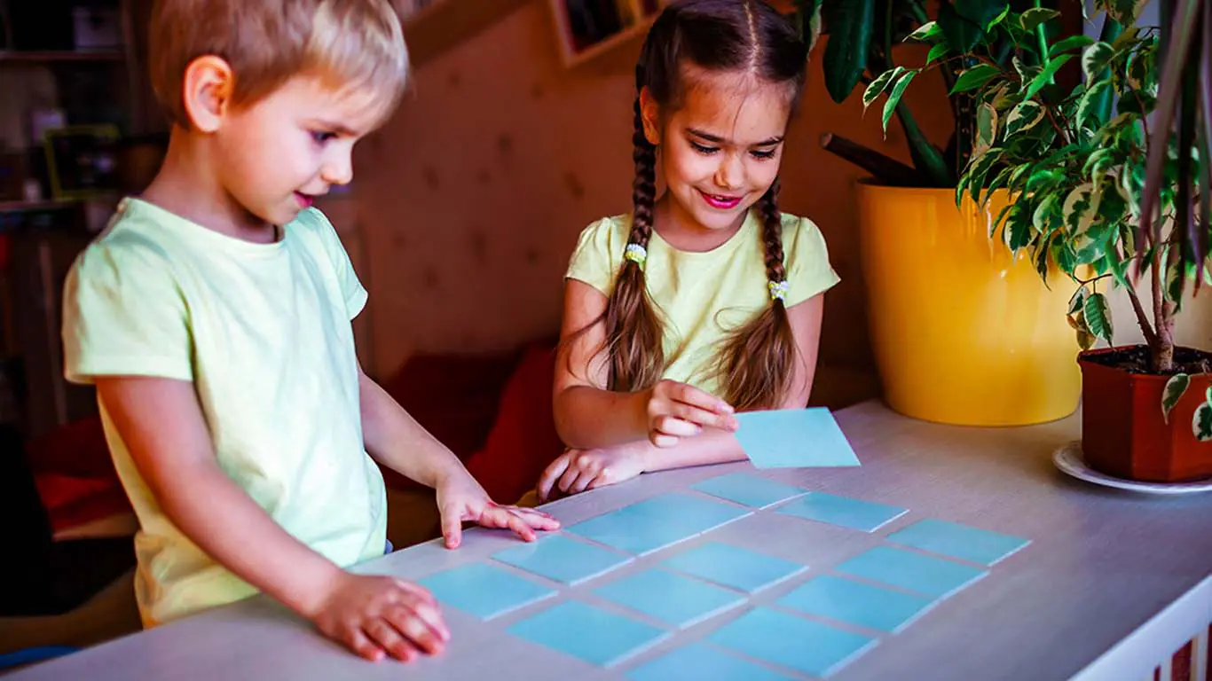Two siblings playing Concentration card game at different difficulty levels, one with cards face-up and one face-down