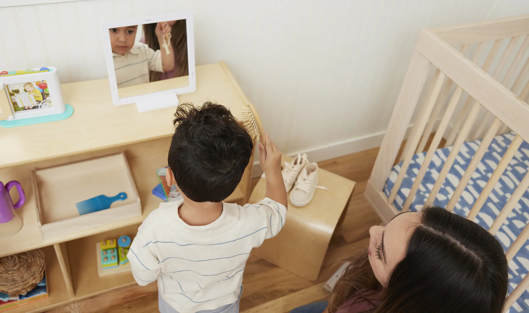 Parent helping toddler put on a shirt using backward chaining method, low shelf Montessori setup